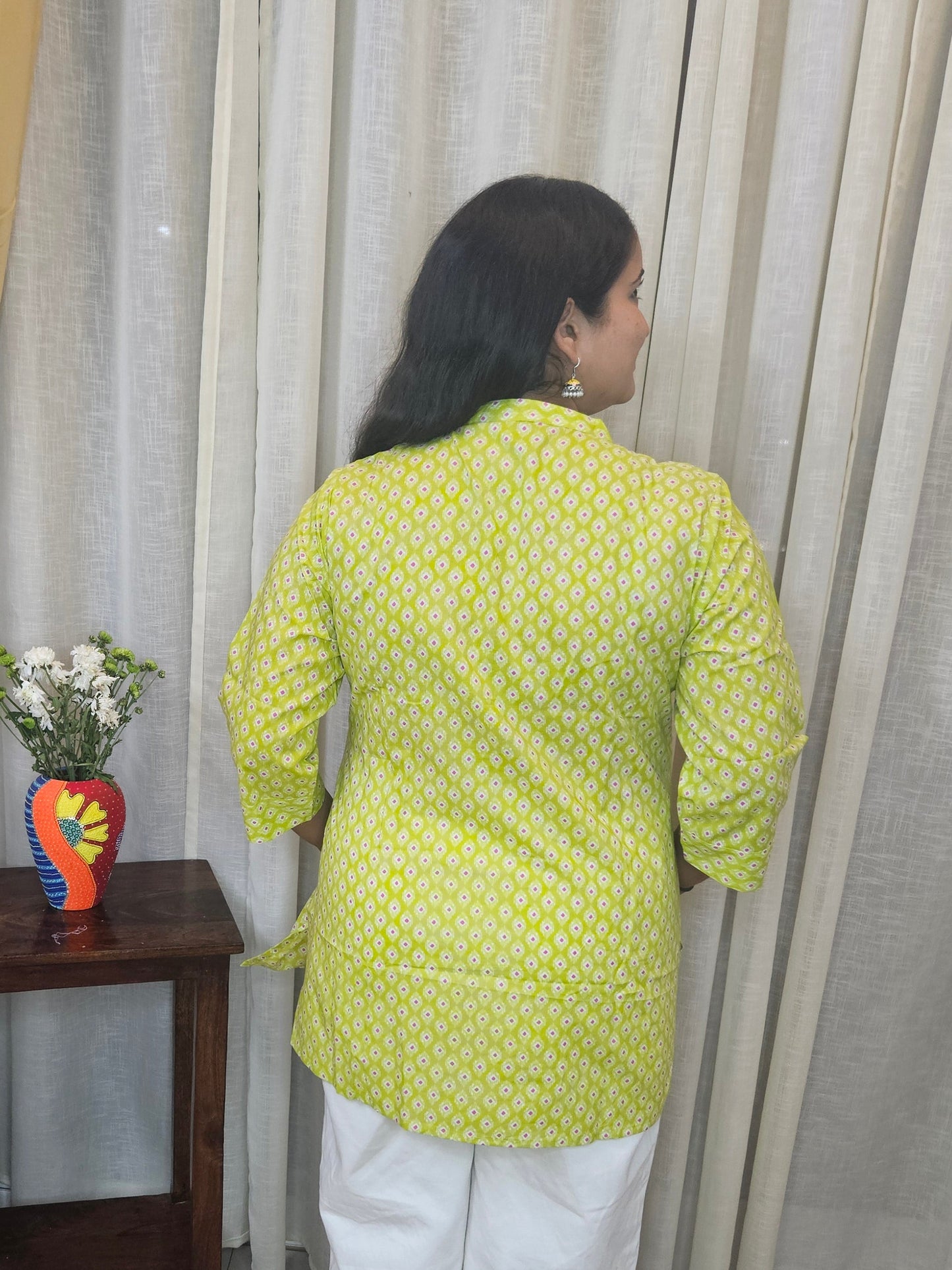 Person in a yellow patterned shirt standing next to a wooden stool with a colorful object on it.