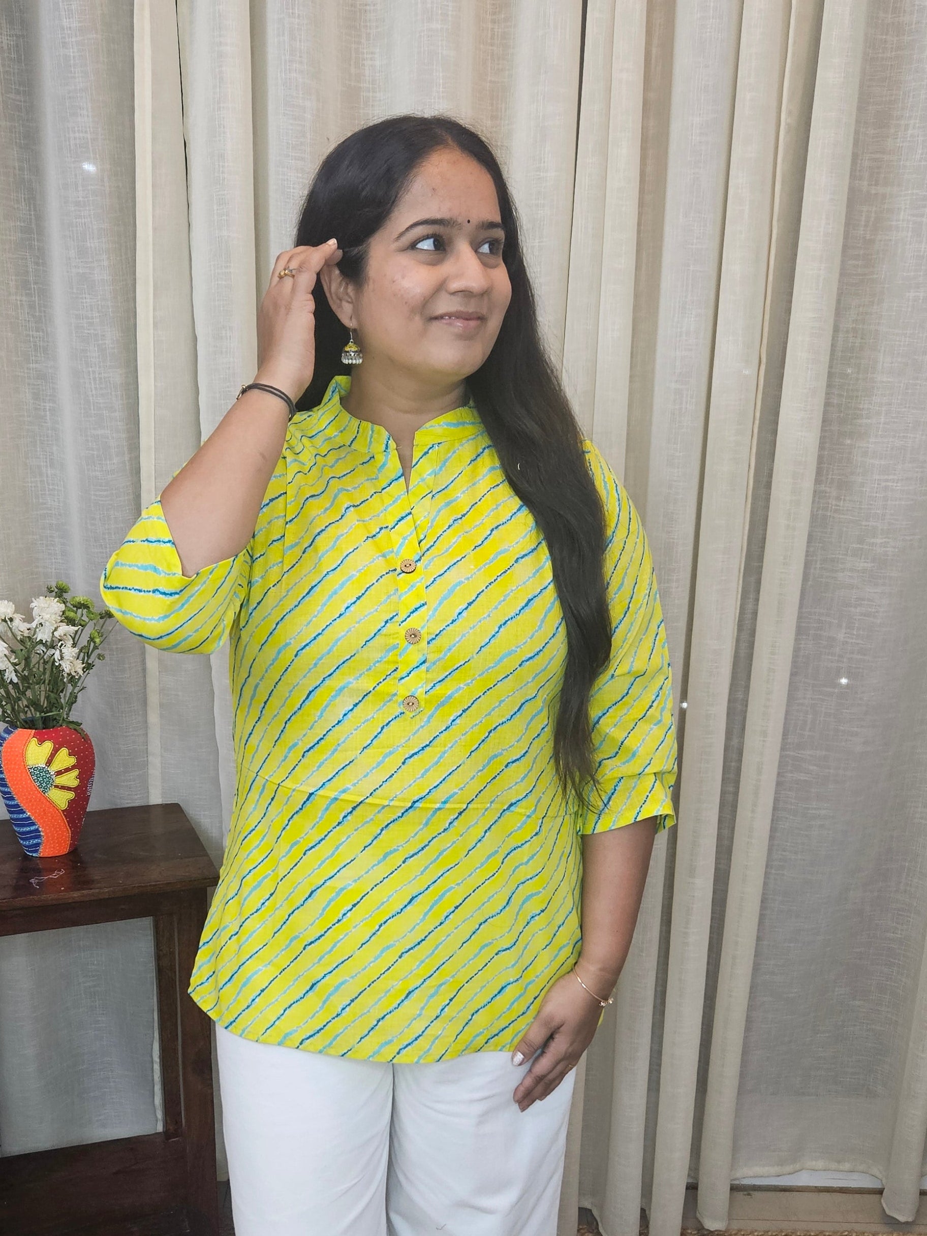 Woman in a yellow top and white pants standing in front of a curtain.
