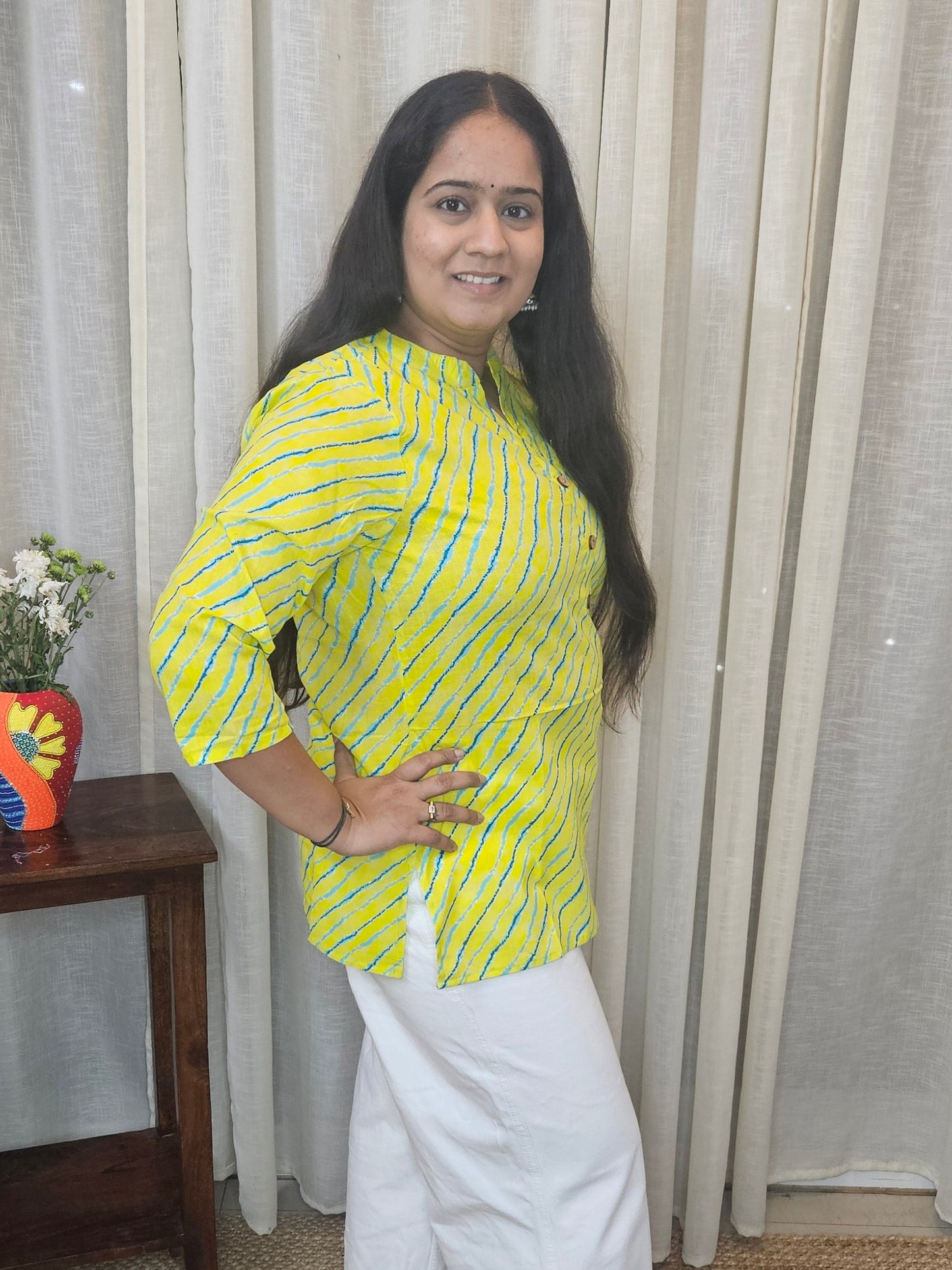 Woman standing in a room with curtains and a small table.